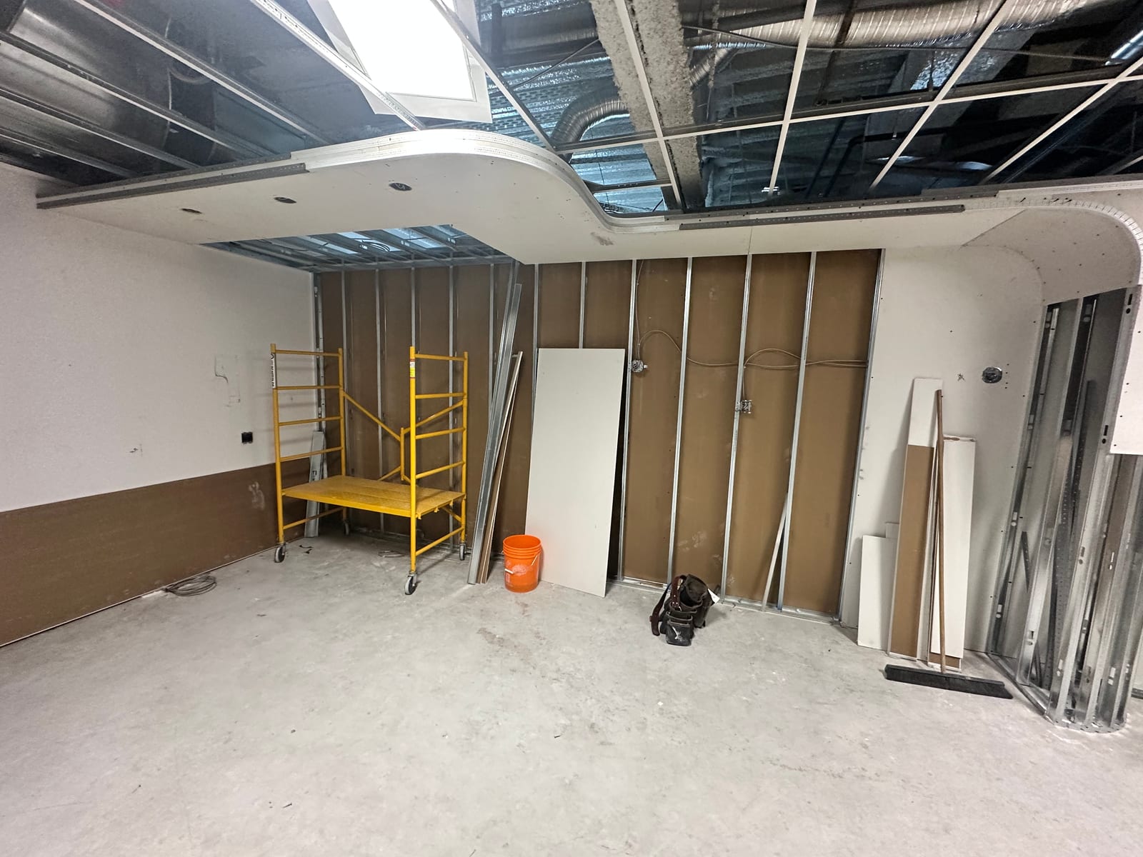 Curved drywall bulkhead with metal framing and T-bar grid in progress